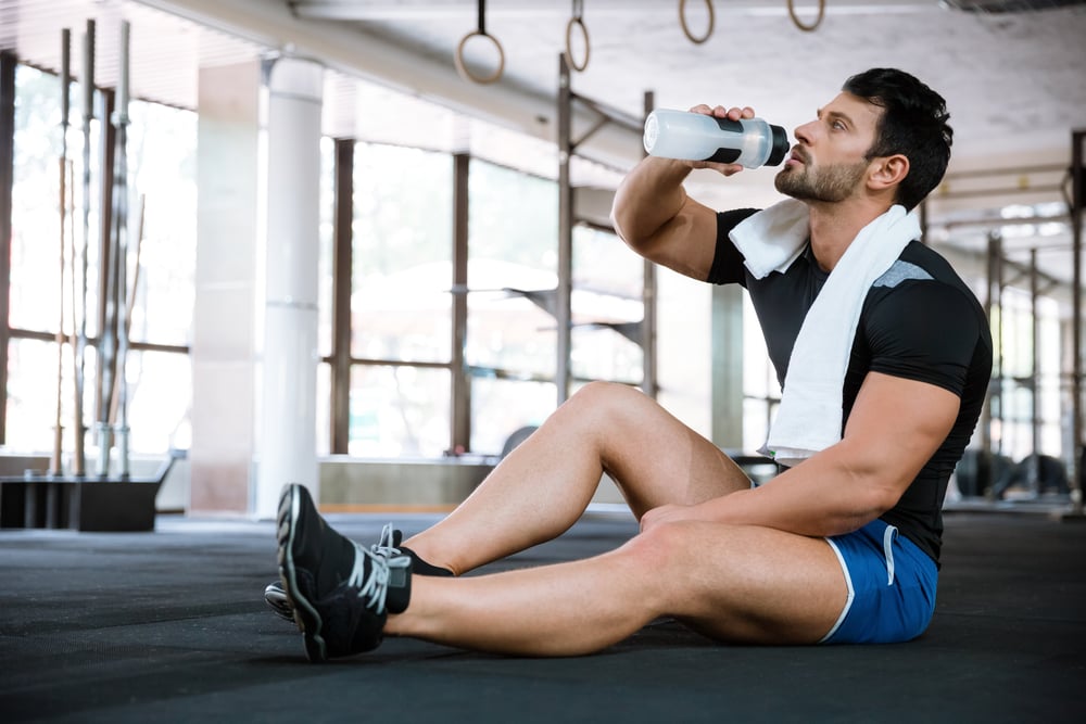 Fitness man sitting on the floor drinking water and resting after a grueling workout