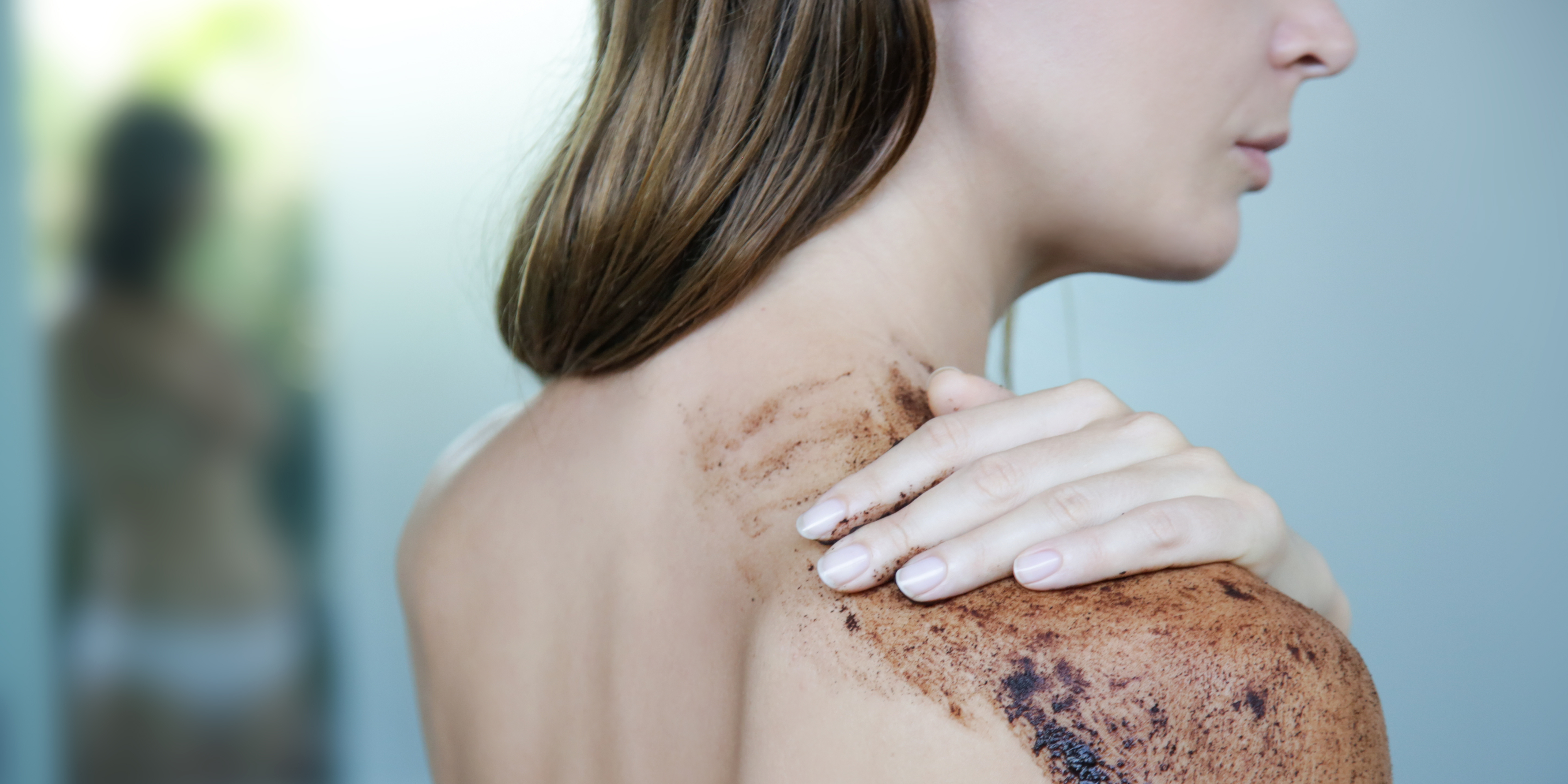 A girl applying coffee scrub on her back.